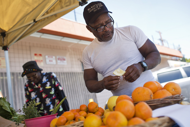 Lou Williams, a regular customer, samples a yellow grapefruit while buying tangerines at the Village Market Place produce stand on Friday, April 10, 2015. | Photo by Maya Sugarman for KPCC